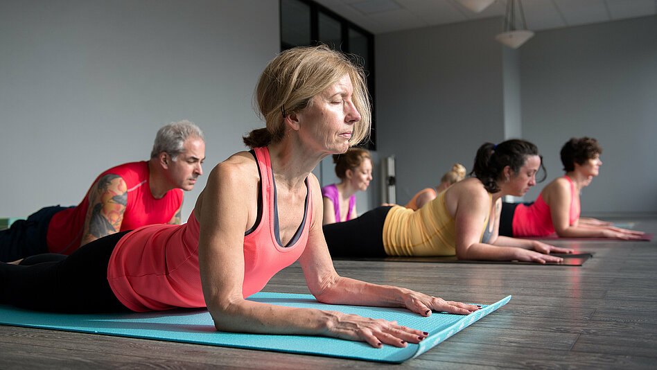 Gruppe mittleren Alters bei einer Yogaübung auf dem Boden.